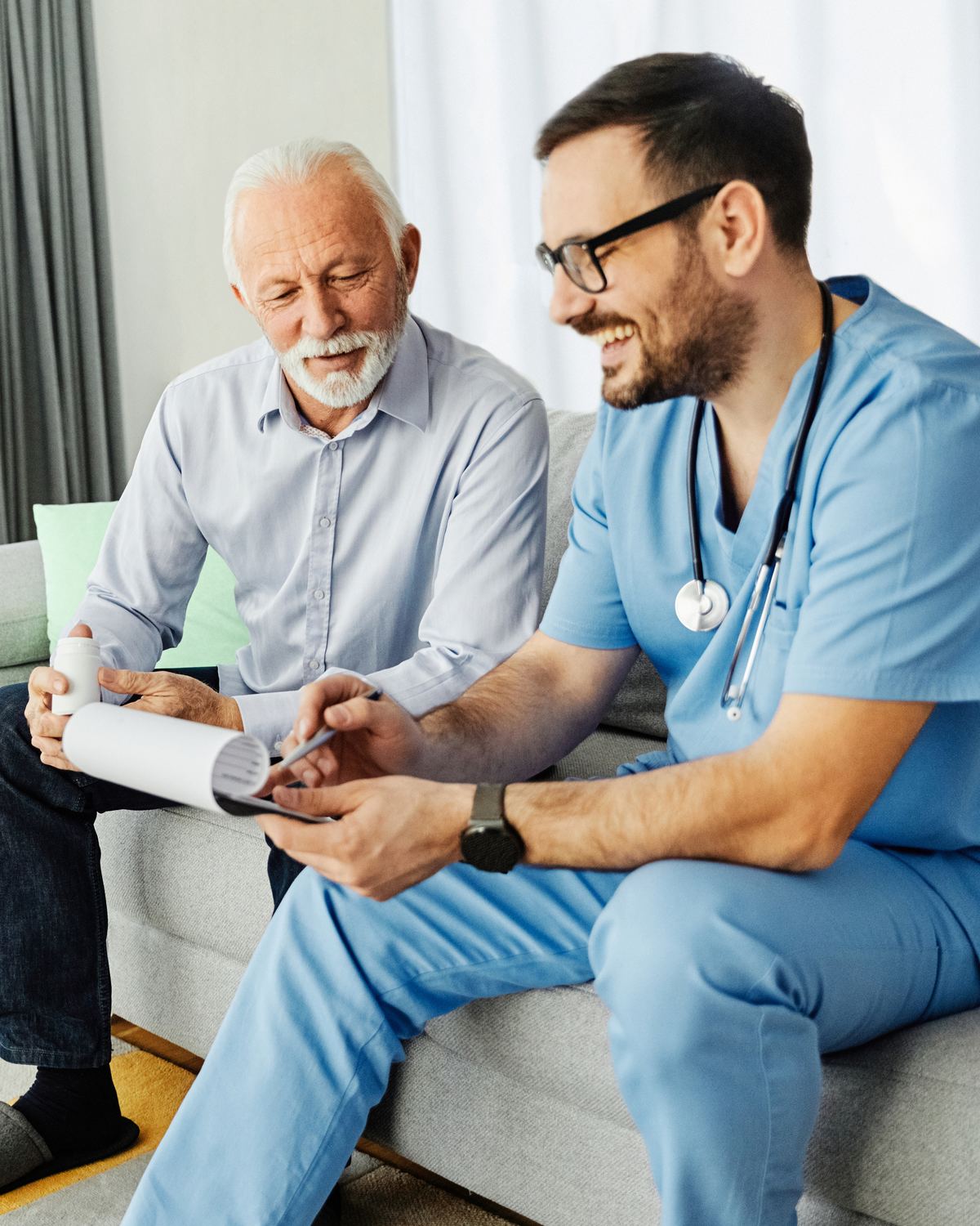 Home health nurse going over care paperwork with an older man on his sofa