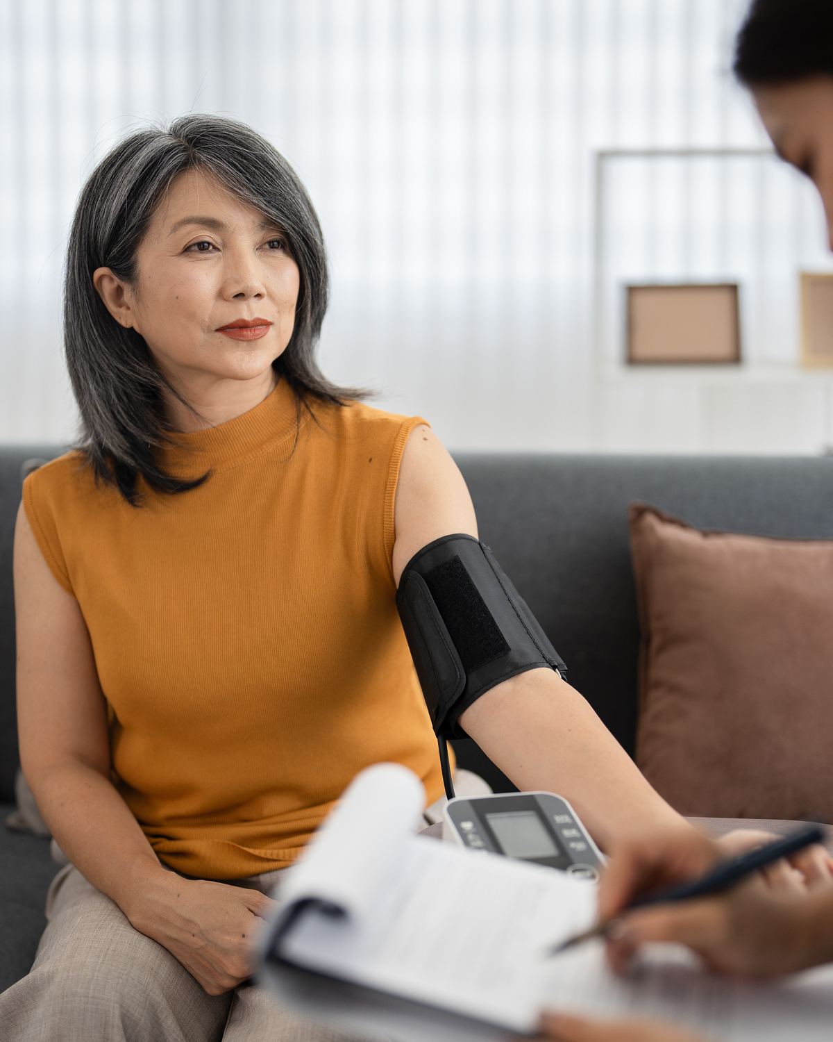 Home health nurse checking a woman's blood pressure on her living room sofa after hospital discharge