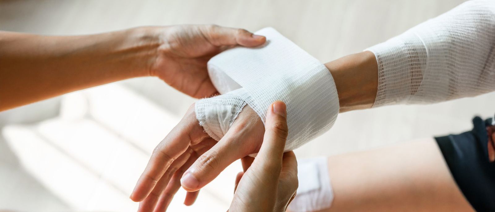 Clinician wrapping a patient's hand and wrist in a fresh bandage during post-surgery wound care at home