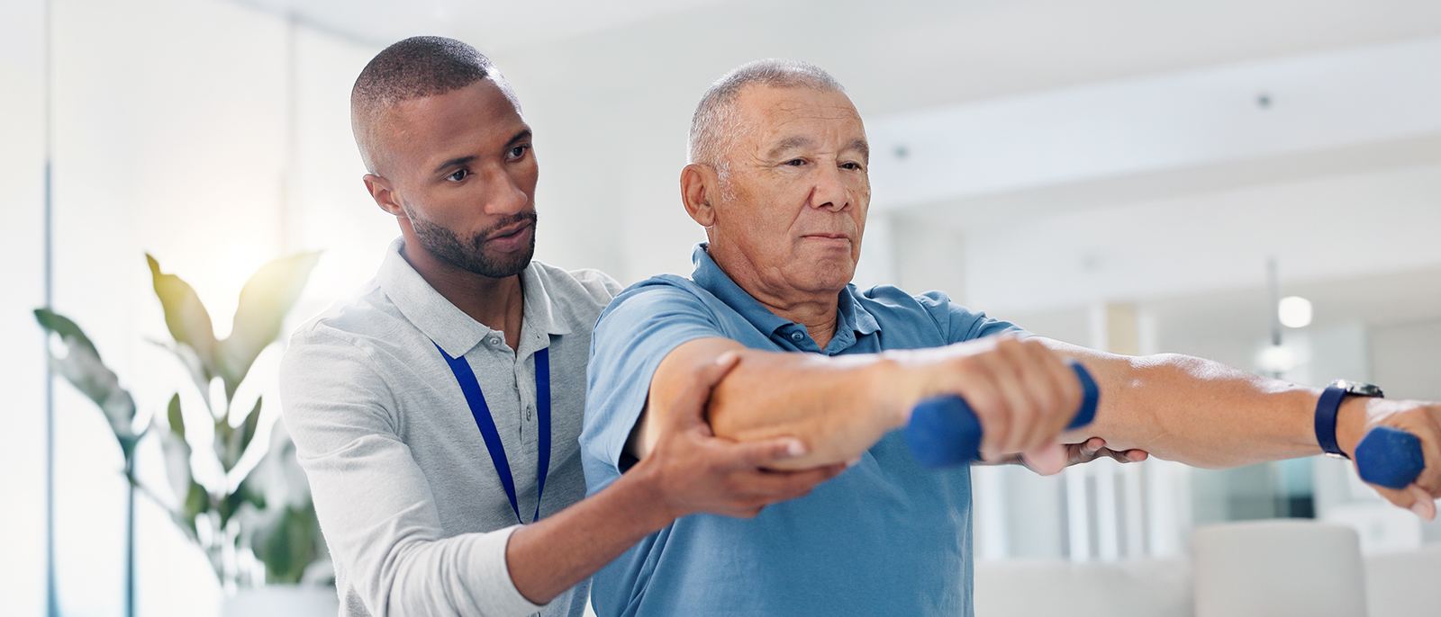 Physical therapist supporting an older man through a light dumbbell exercise